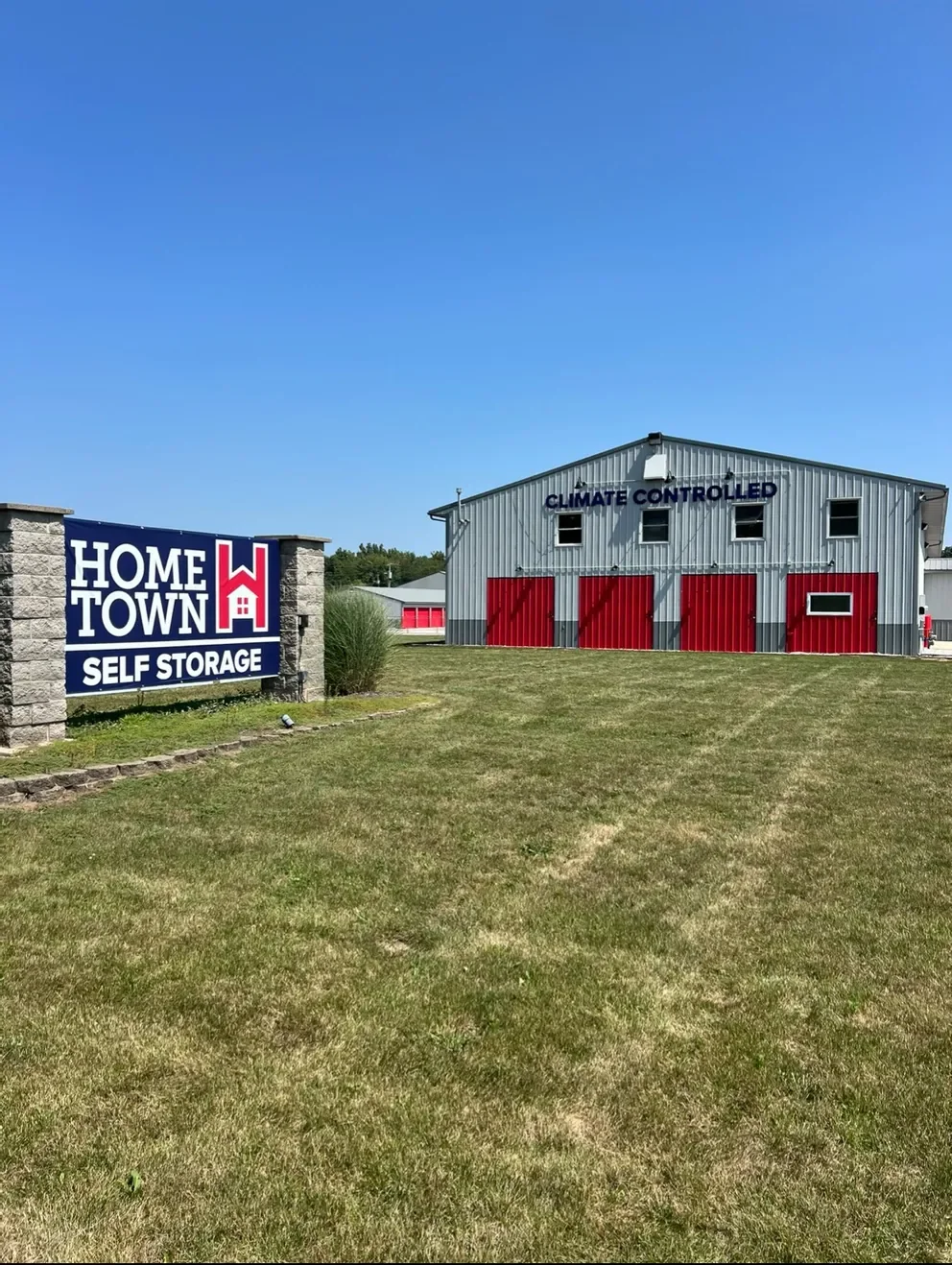 Exterior shot of Hometown Self Storage in North Webster, displaying climate-controlled units with bold red doors. The facility includes a well-maintained lawn and prominent signage, emphasizing high-quality storage solutions.